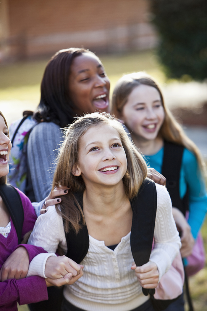 Girls (11-12 years) carrying backpacks standing outside.  Focus on girl in foreground.